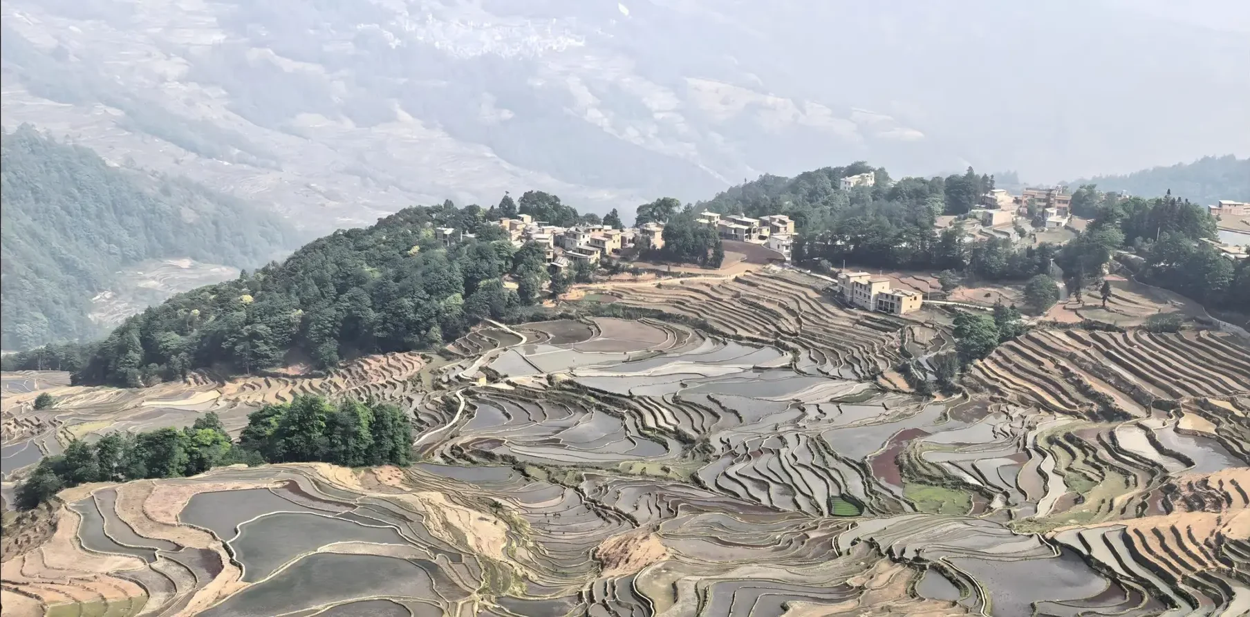 Vue dégagée et vaste paysage des rizières en terrasses de Yuanyang sous un ciel bleu, une destination incontournable au Yunnan.