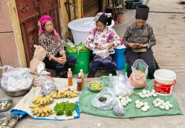 Femmes issues de minorités ethniques en tenues traditionnelles vendant des produits frais sur un marché rural typique du Yunnan.